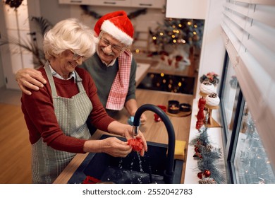 Happy senior couple washing dishes after baking Christmas cookies in the kitchen. - Powered by Shutterstock