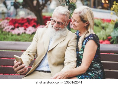 Happy Senior Couple Watching On Mobile Smartphone Outdoor - Mature Fashion Pensioners Having Fun With New Technology Cellphones Apps - Social, Retired, Tech, Elderly Lifestyle Concept