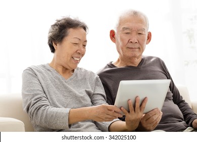 Happy Senior Couple Watching The Tablet On Sofa