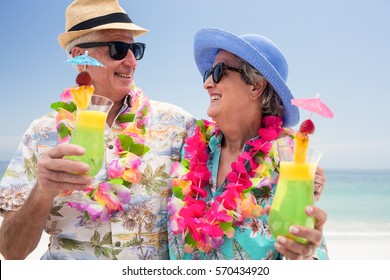 Happy senior couple wearing a garland and holding cocktail glass at the beach - Powered by Shutterstock