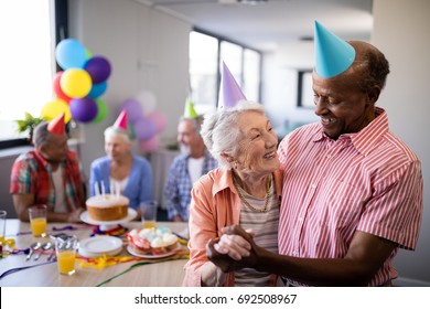 Happy senior couple wearing party hats with friends at birthday celebration - Powered by Shutterstock