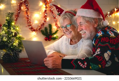 Happy senior couple wearing Santa hat at Christmas time in video call by laptop from home getting in touch with family or friends - Powered by Shutterstock