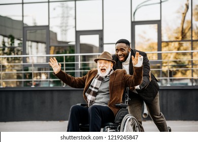 happy senior disabled man in wheelchair and african american man having fun while riding by street