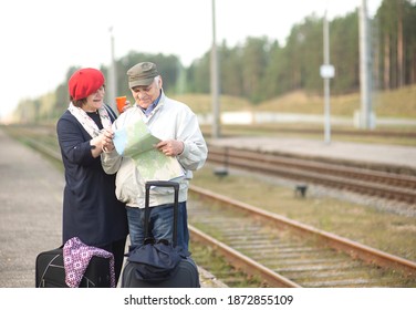 Happy Senior Elderly Couple With Suitcases Looking At The Map And Waiting For The Train To Go On A Trip