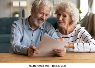 Happy Senior Family Couple Looking At Paper Sheet, Reading Letter With Pleasant News. Smiling Middle Aged Husband And Wife Holding Correspondence Mail Or Medical Insurance Contract Together At Home.