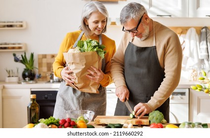 Happy senior family married couple of pensioners cooking healthy vegetarian lunch together in cozy kitchen, smiling elderly wife and husband chopping fresh organic summer vegetables for salad - Powered by Shutterstock