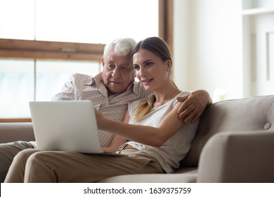 Happy Senior Father Sit Relax On Couch Hug Grownup Daughter Browsing Internet On Laptop Together, Loving Elderly Dad And Adult Female Child Enjoy Weekend At Home Using Wireless Connection On Computer