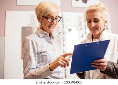 Happy senior female patient consulting with mature optometrist who is holding a clipboard and writing - Powered by Shutterstock