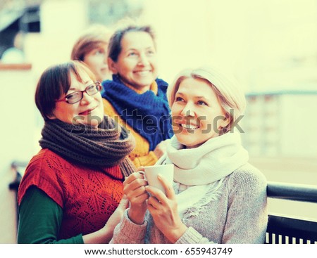 Happy senior female in warm clothes having cup of hot tea on terrace. Focus on blonde woman