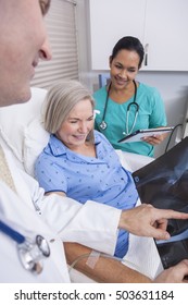 A Happy Senior Female Woman Elderly Patient In Bed Looking At X-ray Of A Hip Replacement With Male Doctor And Hispanic Nurse