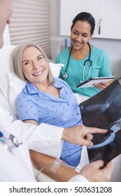 A Happy Senior Female Woman Elderly Patient In Bed Looking At X-ray Of A Hip Replacement Operation With Male Doctor And Hispanic Nurse