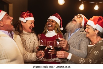 Happy senior friends celebrating Christmas holidays while toasting with red wine glasses on house patio party - Powered by Shutterstock