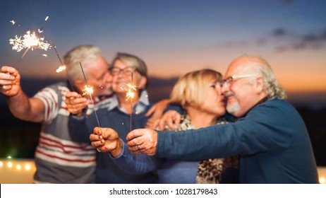 Happy Senior Friends Celebrating With Sparklers Outdoor - Older People Having A Fun And Tender Moment On Rooftop - Love, Party, Elderly Lifestyle Concept