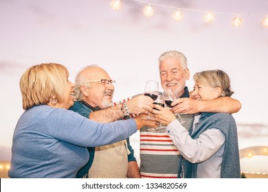 Happy Senior Friends Cheering And Toasting With Red Wine On Terrace - Older People Having Fun At Dinner Party On Patio At Sunset - Friendship, Drink And Elderly Retirement Lifestyle Concept