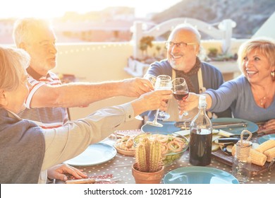 Happy senior friends having fun cheering with red wine at barbecue in terrace outdoor - Older people making  dinner toasting glasses and laughing together - Friendship and elderly lifestyle concept  - Powered by Shutterstock