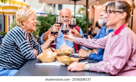 Happy senior friends having fun toasting and drinking red wine at dinner party - Retired people eating at restaurant patio together - Dining lifestyle concept with pensioners having fun together - Powered by Shutterstock