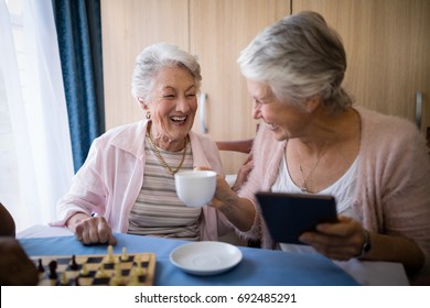 Happy senior friends talking while having coffee and playing chess at nursing home - Powered by Shutterstock