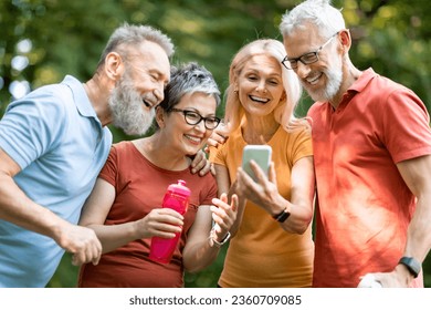 Happy Senior Friends Using Smartphone Together While Relaxing Outdoors After Training, Smiling Elderly People In Sportswear Watching Photos On Mobile Phone, Resting After Fitness Workout Outside - Powered by Shutterstock