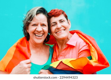 Happy Senior gay lesbian couple having fun wearing Lgbtq rainbow flag at pride parade - Family and love concept - Focus on right woman face - Powered by Shutterstock