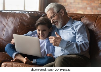 Happy senior grandfather with little grandson using laptop together, sitting on couch at home, smiling mature grandpa and 8s boy kid making video call, chatting online, looking at computer screen - Powered by Shutterstock