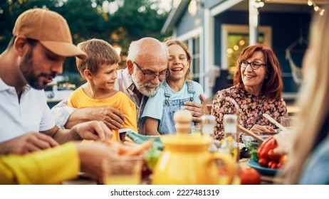 Happy Senior Grandfather Talking and Having Fun with His Grandchildren, Holding Them on Lap at a Outdoors Dinner with Food and Drinks. Adults at a Garden Party Together with Kids. - Powered by Shutterstock