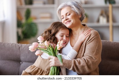 Happy senior grandmother with bouquet of flowers    gently hugs his  cute little granddaughter, receiving congratulations and a gift from her  from  while getting hollyday on grandparents day - Powered by Shutterstock