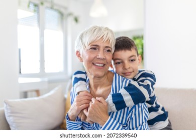 Happy senior grandmother sit on couch in living room hugging cute little preschooler grandson, smiling mature 70s granny embrace cuddle with small grandchild, show love and care, bonding concept