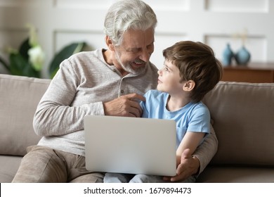 Happy senior grandparent relax on sofa in living room with small grandson use laptop together, smiling grandfather rest on couch at home with little grandchild have fun watch video on computer - Shutterstock ID 1679894473
