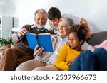 Happy senior grandparents having fun, reading book to multiethnic grandchildren.