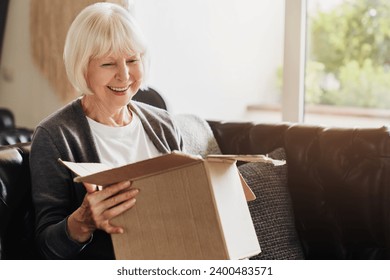 Happy senior grey-haired woman sitting on couch opening carton box received parcel package, internet order, medical goods, pills, vitamins, medications, drugs. - Powered by Shutterstock