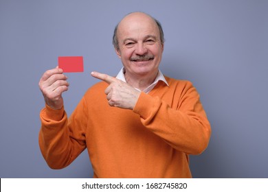 Happy Senior Hispanic Bald Man Advertising Bonus Card Pointing On It With Finger Smiling At Camera. Guy Going To Pay By Credit Card, Doing Shopping