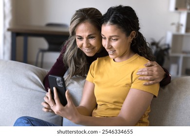 Happy senior Hispanic mom and adult daughter girl browsing social media on smartphone together, using online technology, application on mobile phone at home, watching Internet content - Powered by Shutterstock