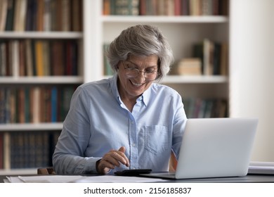 Happy Senior Homeowner Woman In Glasses Using Calculator, Laptop Computer For Accounting Work, Counting Budget, Calculating Taxes, Insurance Fees, Paying Bills With Internet App