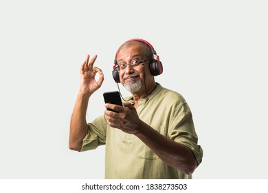 Happy Senior Indian Asian Bearded Man Smiling Using Headphones With Smartphone Or Tablet Against White Background, Presenting Screen Or Dancing