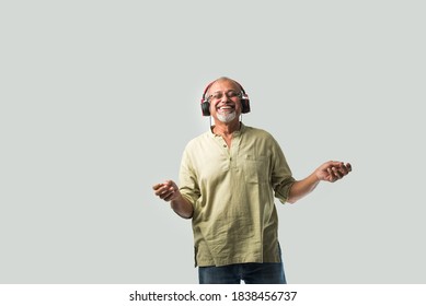 happy senior Indian asian bearded man smiling using headphones with smartphone or tablet against white background, presenting screen or dancing