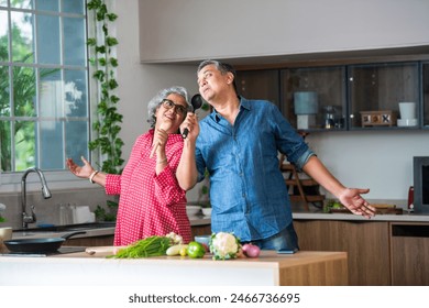 Happy senior Indian asian couple husband and wife have fun sing in kitchen appliances cooking together at home. - Powered by Shutterstock