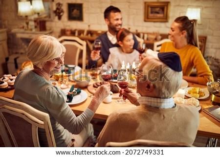 Happy senior Jewish couple toasting with wine during family dinner on Hanukkah.