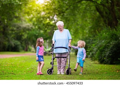 Happy senior lady with a walker holding hands of little boy and girl. Grandmother with grand children enjoy a walk in summer park. Kids supporting disabled grandparent.