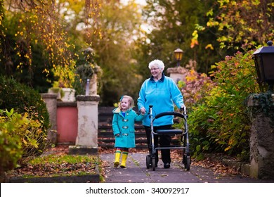 Happy Senior Lady With A Walker Or Wheel Chair And Children. Grandmother And Kids Enjoying A Walk In The Park. Child Supporting Disabled Grandparent. Family Visit. Generations Love And Relationship.