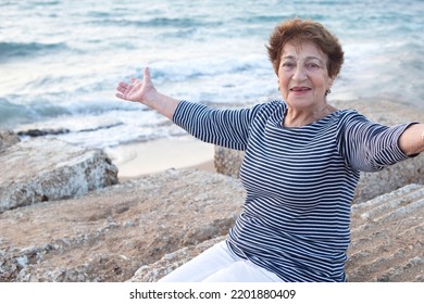 Happy Senior Lady, Woman 75+ At The Seaside With Arms Wide Open. Concept Of Happiness, Health Insurance, Quality Of Life, Travel In Old Age, Cheerful Grandmother. Caucasian. Emotional Smiling Face.