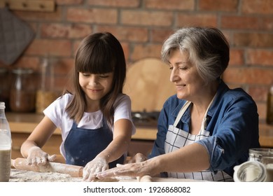 Happy Senior Latino Grandmother And Little Granddaughter Make Dough Bake Cookies Or Pastries Together. Smiling Mature Hispanic Granny Help Small Grandchild Teach Cooking At Home Kitchen.