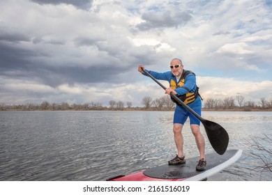 Happy Senior Male Paddler On A Stand Up Paddleboard, Lake In Colorado In Early Spring Scenery