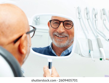 Happy senior man admiring his new smile in the small mirror at the dental clinic after a successful surgery