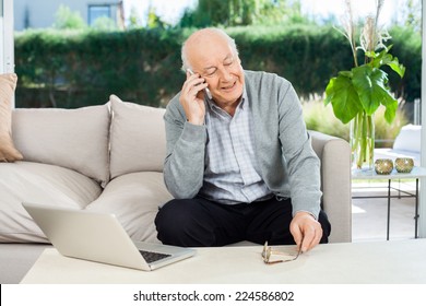Happy senior man answering smartphone while sitting on couch at nursing home porch