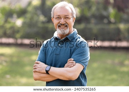 Happy senior man with arms crossed at park