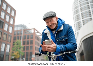 Happy senior man with bicycle outdoors on street in city, using smartphone.
