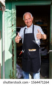 Happy Senior Man In Black Apron Standing In Doorway Of His Garden Shed
