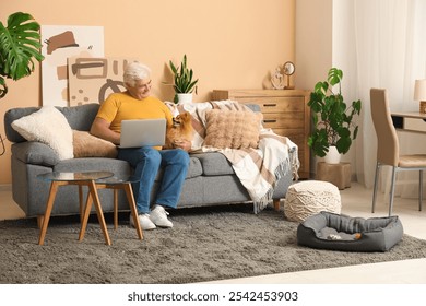 Happy senior man with cute Pomeranian dog and laptop sitting on sofa at home - Powered by Shutterstock