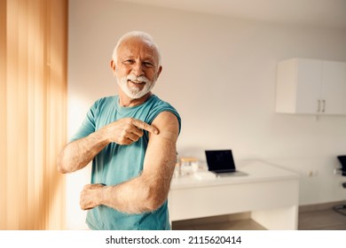 A Happy Senior Man In Doctor's Office Pointing At His Vaccinated Shoulder. Immunization And Vaccination.