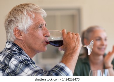 Happy senior man drinking a glass of red wine during lunch. Old man enjoying wine with friends in background. Closeup face of active and healthy senior man tasting wine. - Powered by Shutterstock